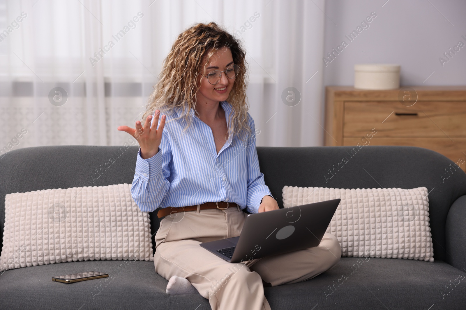 Smiling woman having videochat by laptop on sofa in home office Photo of Smiling woman having videochat by laptop on sofa in home office