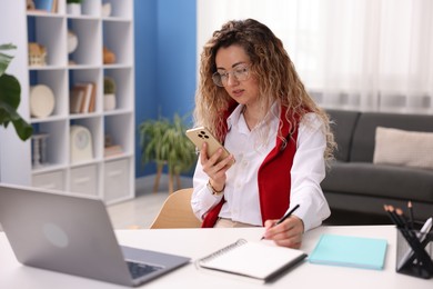 Photo of Woman with smartphone working at desk in home office