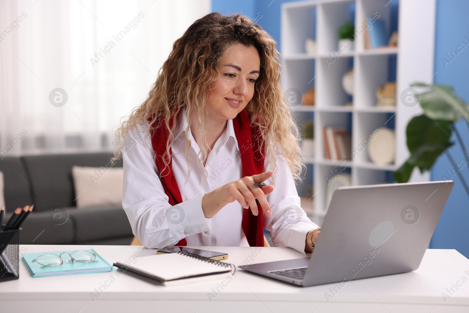 Smiling woman having videochat by laptop at desk in home office Photo of Smiling woman having videochat by laptop at desk in home office