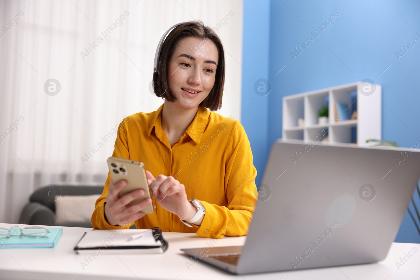 Smiling woman with smartphone and laptop working at desk in home office Photo of Smiling woman with smartphone and laptop working at desk in home office