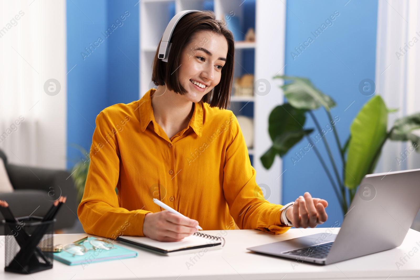 Smiling woman in headphones having videochat by laptop at desk in home office Photo of Smiling woman in headphones having videochat by laptop at desk in home office