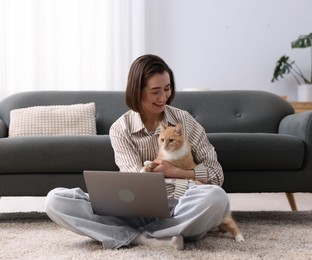 Photo of Smiling woman working with laptop and cat on floor in home office
