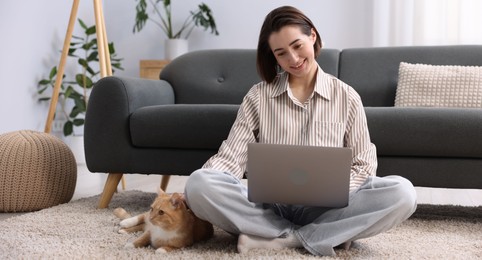 Photo of Smiling woman working with laptop and cat on floor in home office