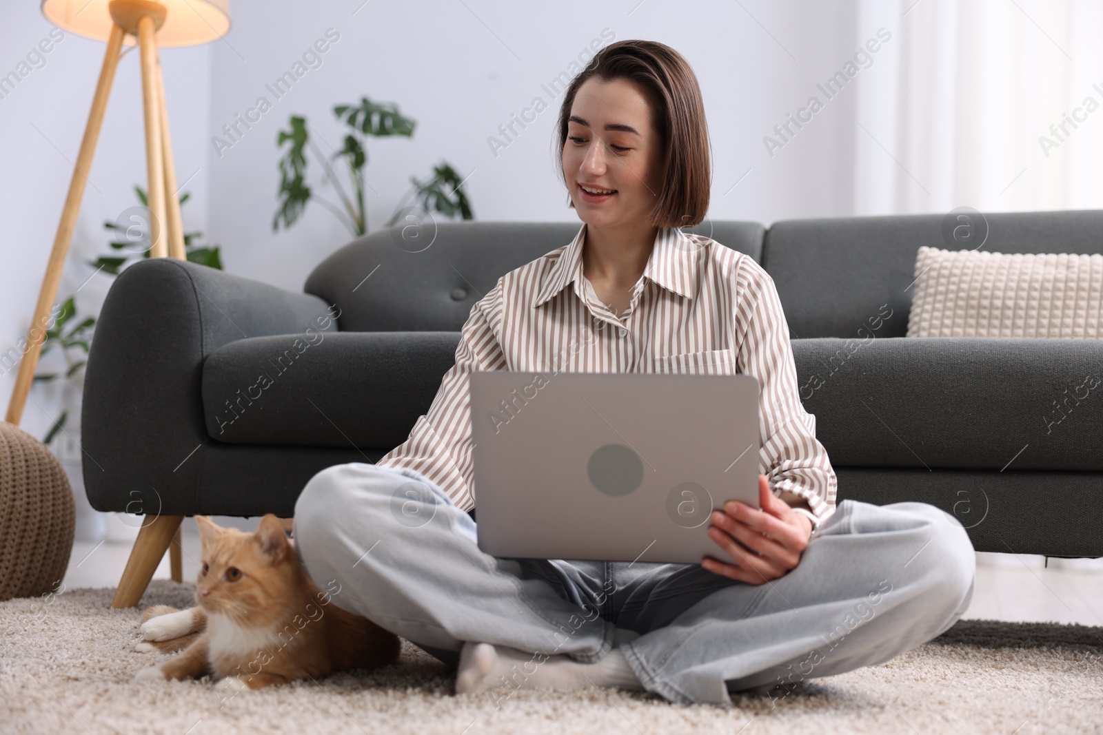 Smiling woman working with laptop and cat on floor in home office Photo of Smiling woman working with laptop and cat on floor in home office