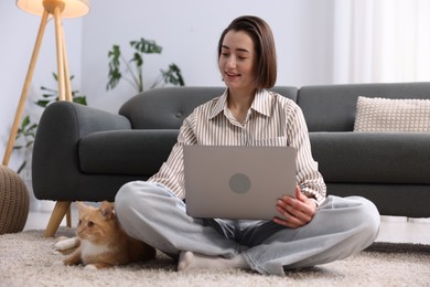 Photo of Smiling woman working with laptop and cat on floor in home office