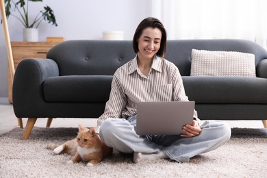 Photo of Smiling woman working with laptop and cat on floor in home office