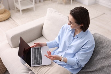 Photo of Woman having videochat by laptop on sofa in home office