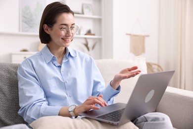 Photo of Smiling woman having videochat by laptop on sofa in home office