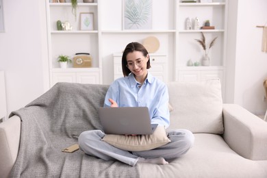 Photo of Smiling woman having videochat by laptop on sofa in home office