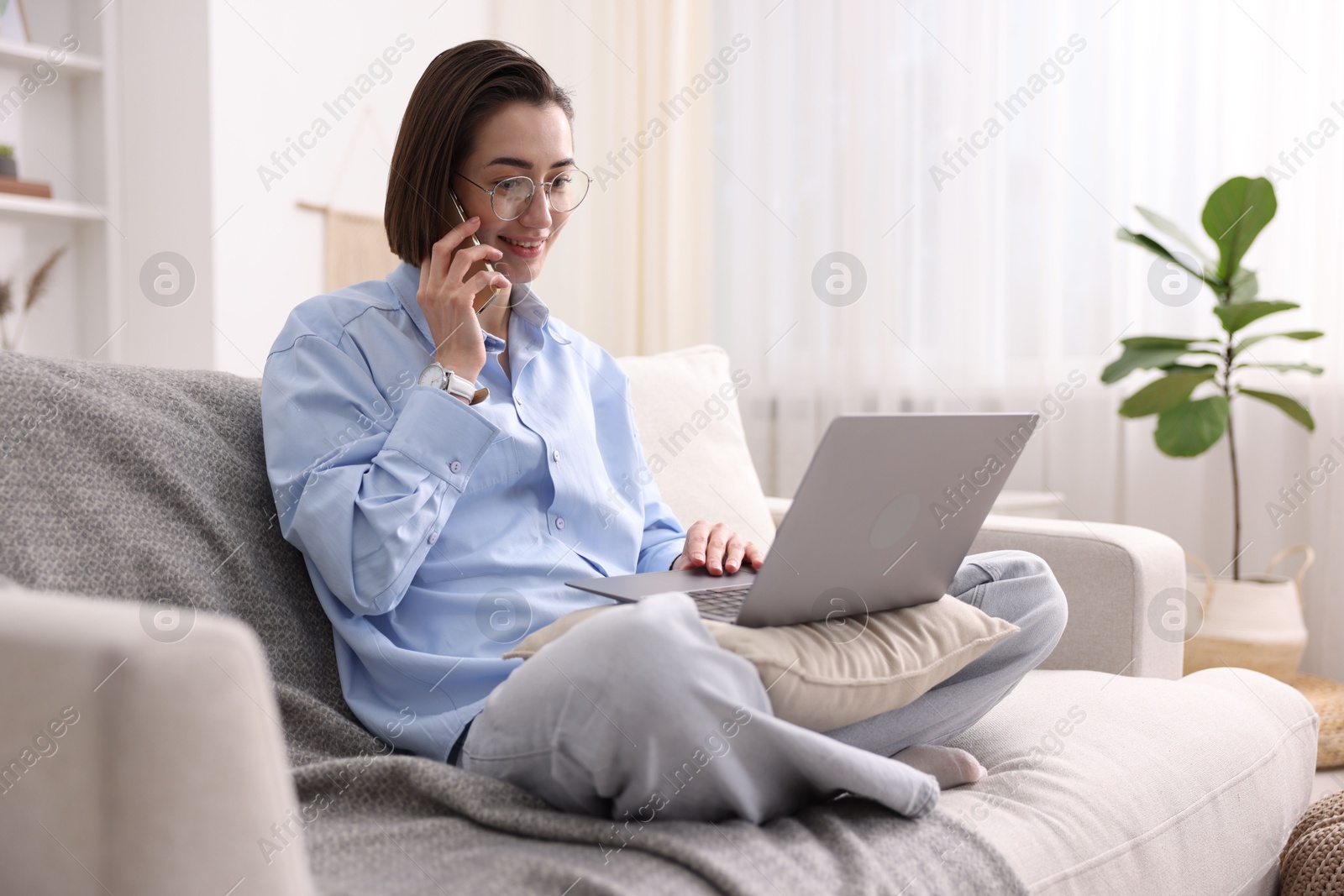 Smiling woman talking by smartphone with laptop on sofa in home office Photo of Smiling woman talking by smartphone with laptop on sofa in home office