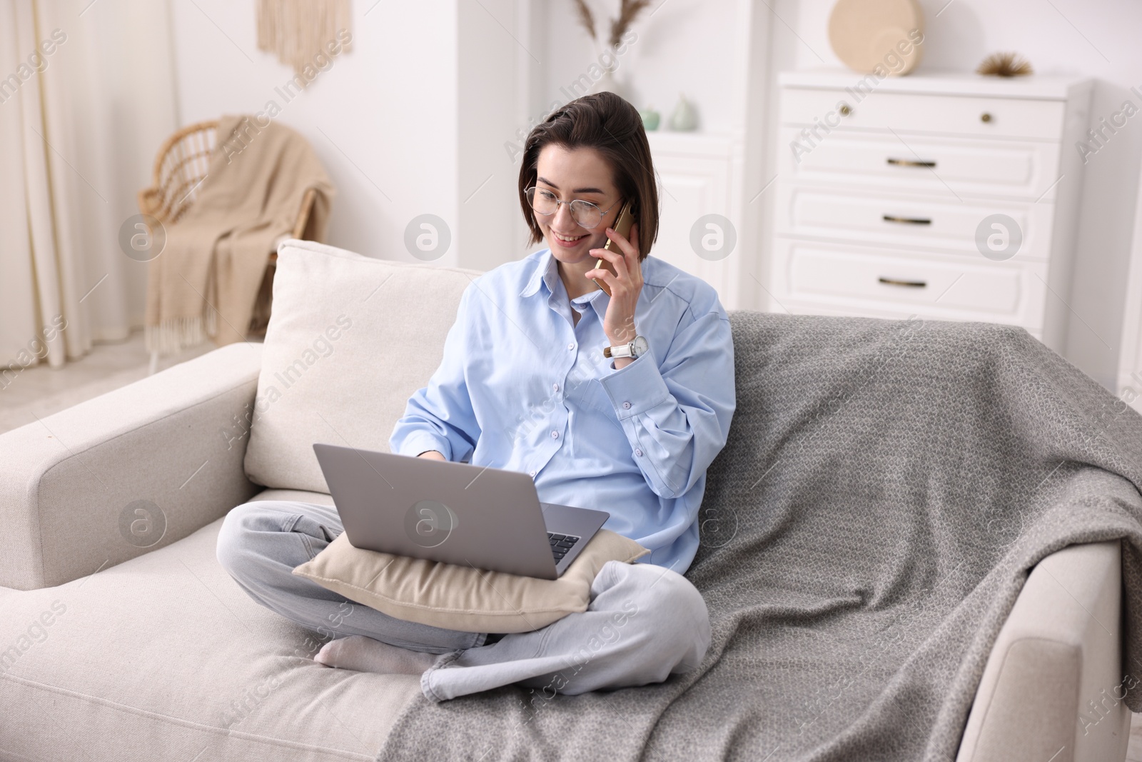 Smiling woman talking by smartphone with laptop on sofa in home office Photo of Smiling woman talking by smartphone with laptop on sofa in home office