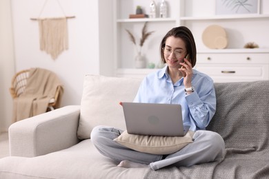 Photo of Smiling woman talking by smartphone with laptop on sofa in home office