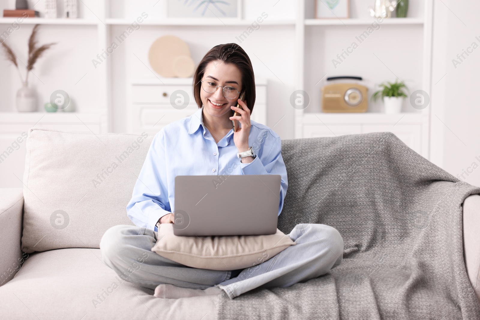 Smiling woman talking by smartphone with laptop on sofa in home office Photo of Smiling woman talking by smartphone with laptop on sofa in home office