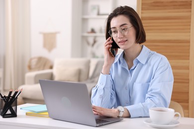 Photo of Woman talking by smartphone with laptop at desk in home office