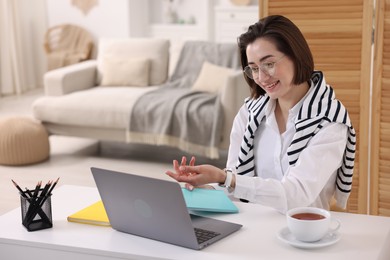 Photo of Smiling woman having videochat by laptop at desk in home office