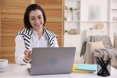 Photo of Smiling woman having videochat by laptop at desk in home office