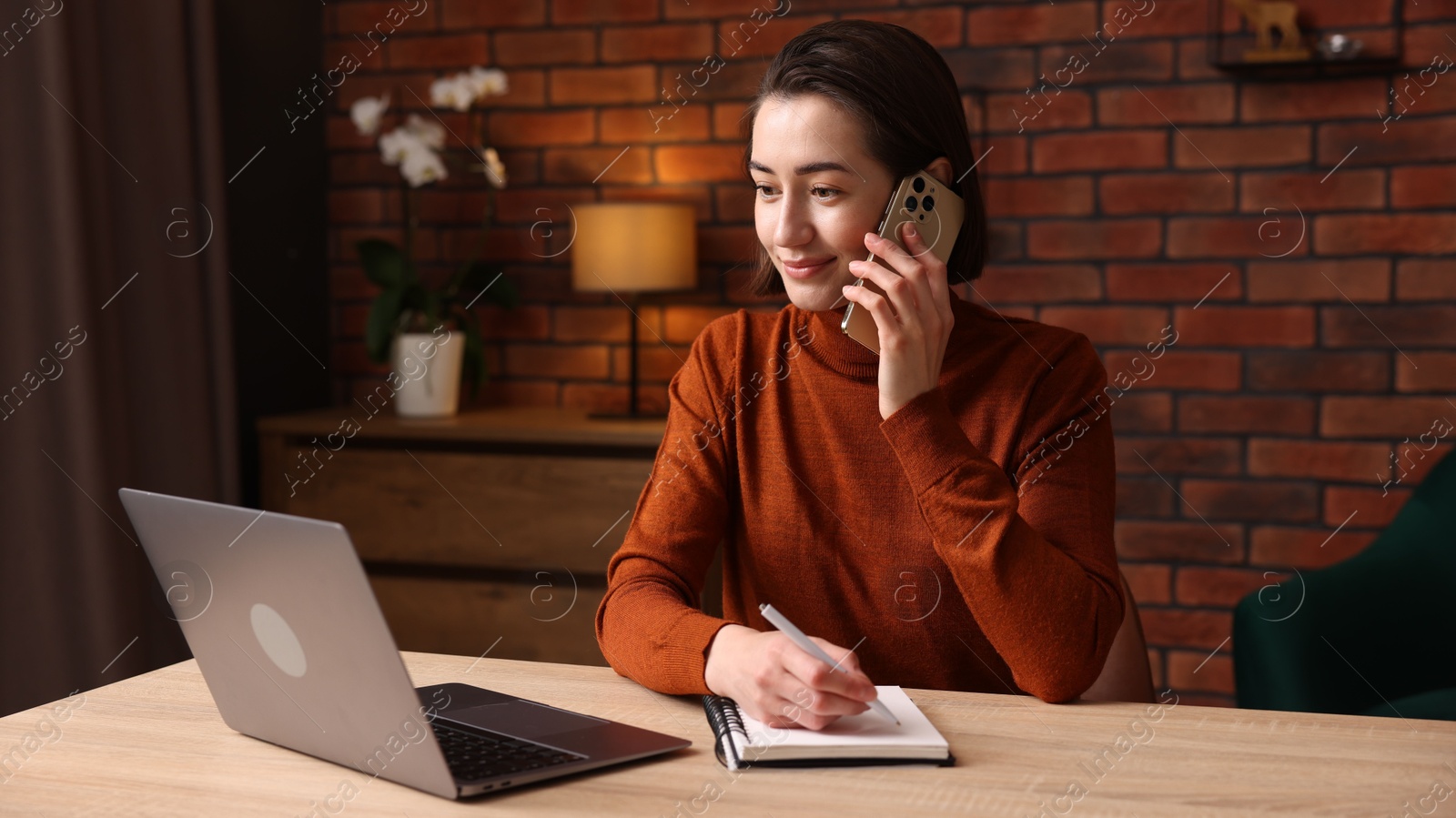 Woman talking by smartphone and working at desk in home office Photo of Woman talking by smartphone and working at desk in home office