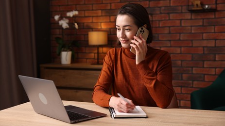 Photo of Woman talking by smartphone and working at desk in home office