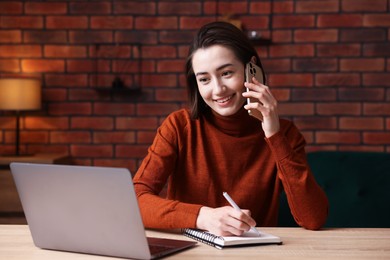 Photo of Smiling woman talking by smartphone and working at desk in home office
