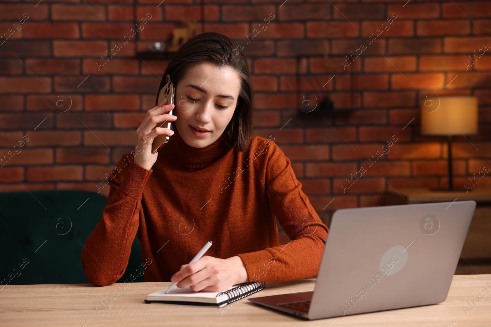 Woman talking by smartphone and working at desk in home office Photo of Woman talking by smartphone and working at desk in home office