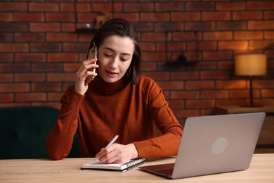 Photo of Woman talking by smartphone and working at desk in home office