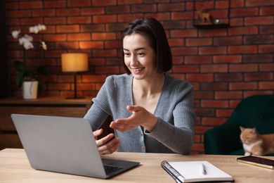 Photo of Smiling woman having videochat by laptop at desk in home office