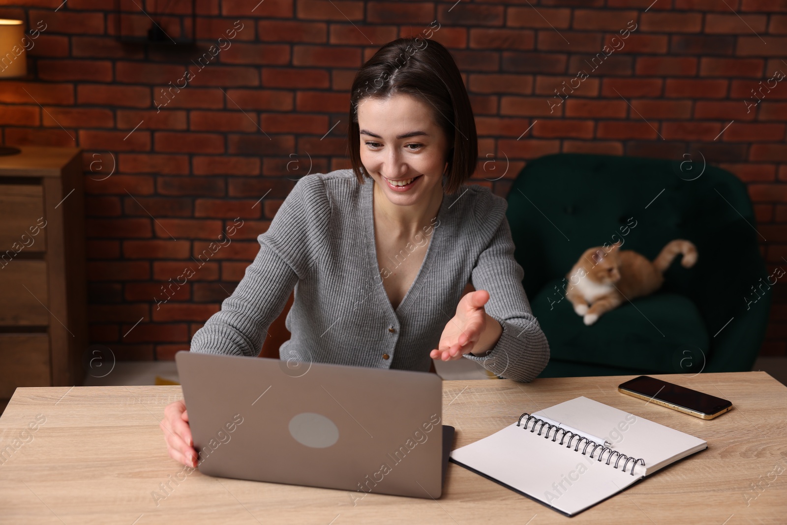 Smiling woman having videochat by laptop at desk in home office Photo of Smiling woman having videochat by laptop at desk in home office
