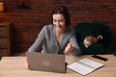 Photo of Smiling woman having videochat by laptop at desk in home office
