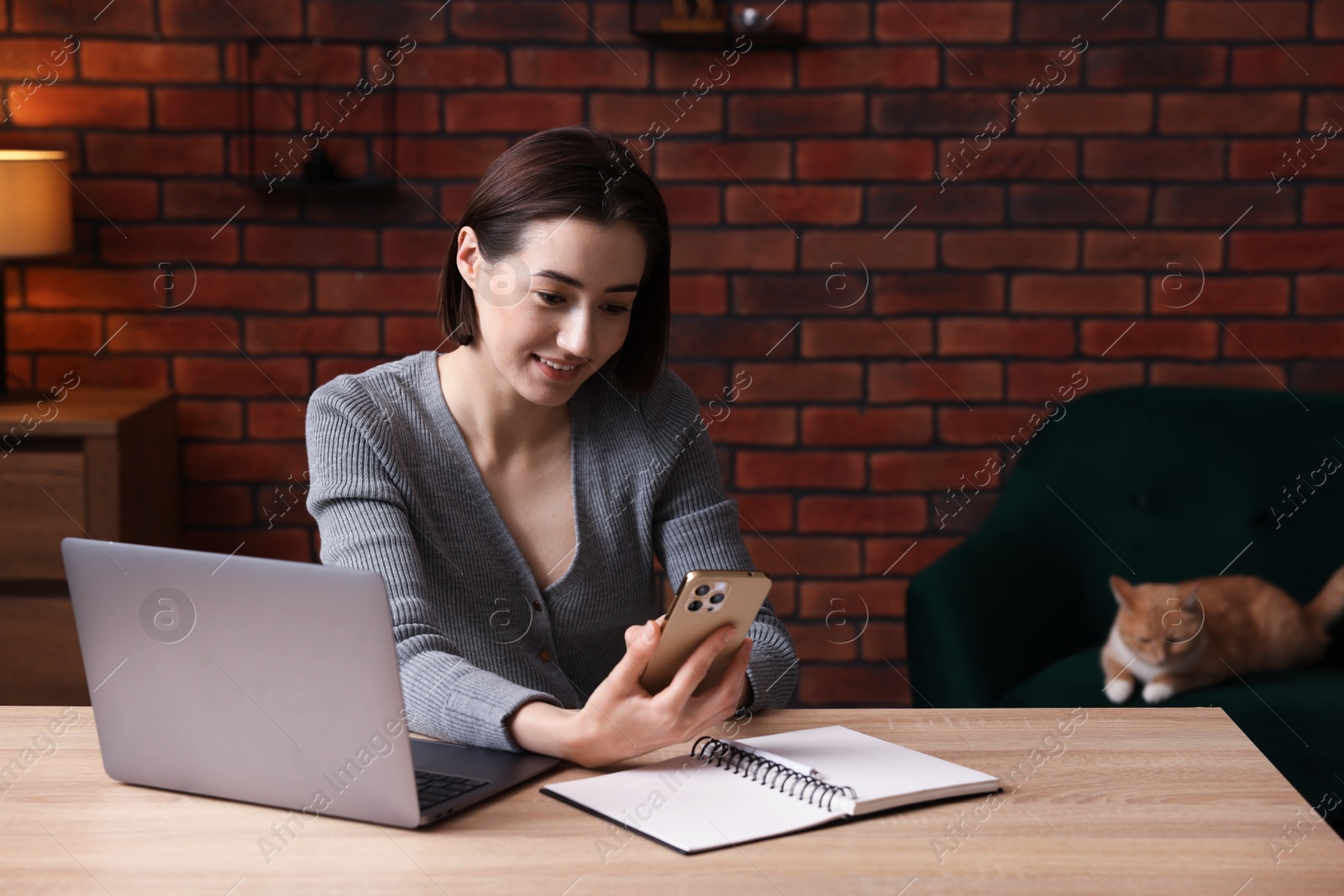 Smiling woman working with smartphone and laptop at desk in home office Photo of Smiling woman working with smartphone and laptop at desk in home office