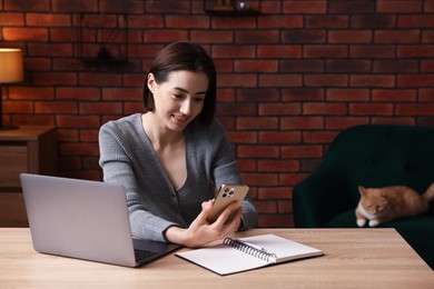 Photo of Smiling woman working with smartphone and laptop at desk in home office