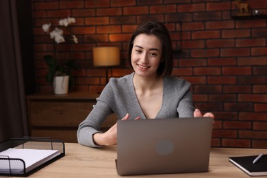 Photo of Smiling woman having videochat by laptop at desk in home office