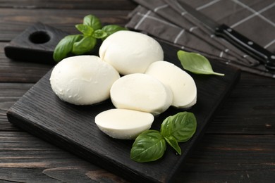 Photo of Pieces of delicious mozzarella cheese and basil in bowl on wooden table, closeup