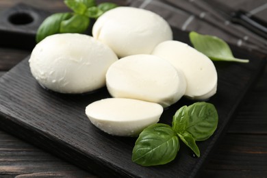 Photo of Pieces of delicious mozzarella cheese and basil in bowl on wooden table, closeup