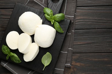 Photo of Pieces of delicious mozzarella cheese and basil on wooden table, top view. Space for text