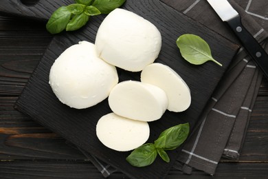 Photo of Pieces of delicious mozzarella cheese and basil on wooden table, flat lay