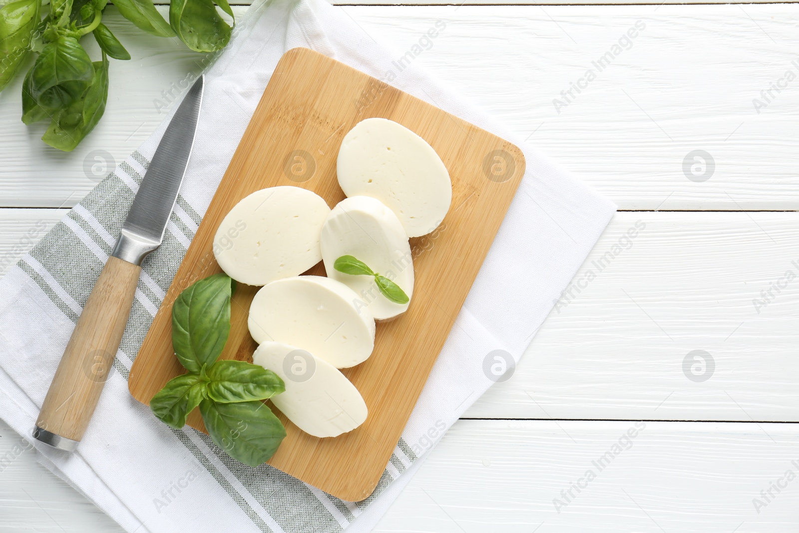 Pieces of delicious mozzarella cheese, basil leaves and knife on white wooden table, flat lay. Space for text Photo of Pieces of delicious mozzarella cheese, basil leaves and knife on white wooden table, flat lay. Space for text