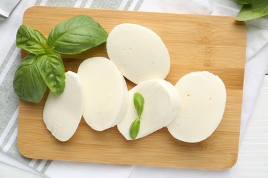 Photo of Pieces of delicious mozzarella cheese and basil on white wooden table, flat lay