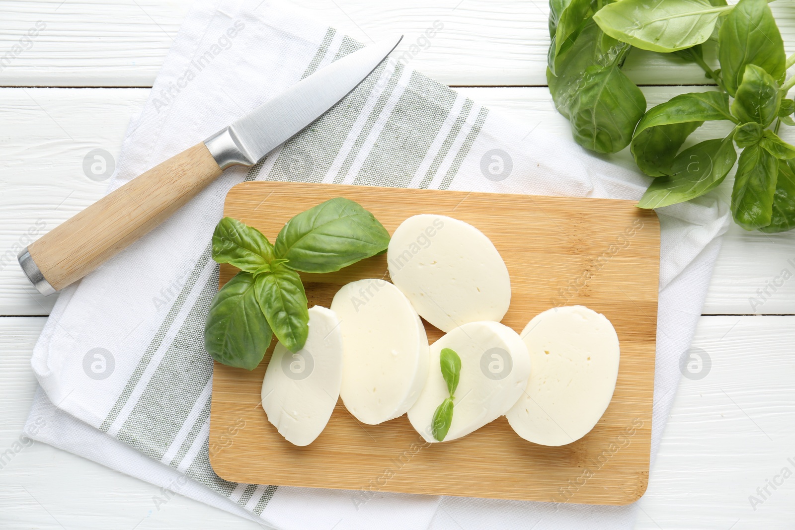 Pieces of delicious mozzarella cheese, basil leaves and knife on white wooden table, flat lay Photo of Pieces of delicious mozzarella cheese, basil leaves and knife on white wooden table, flat lay