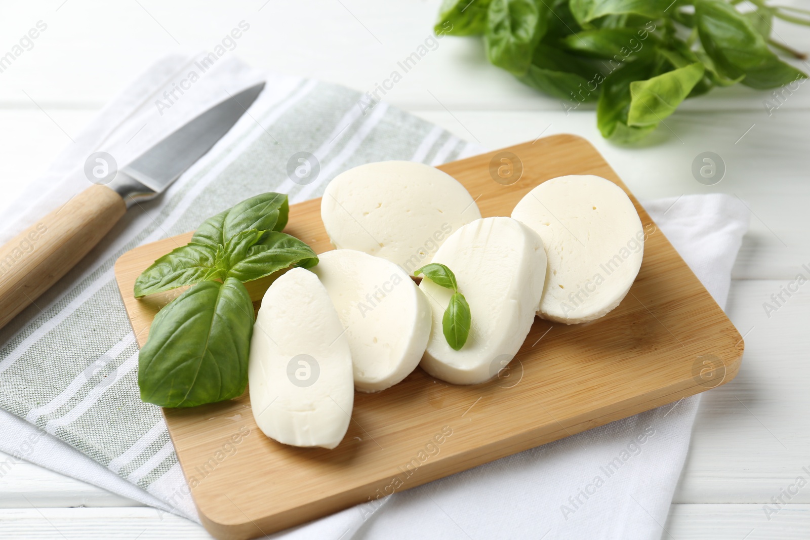 Pieces of delicious mozzarella cheese, basil leaves and knife on white wooden table, closeup Photo of Pieces of delicious mozzarella cheese, basil leaves and knife on white wooden table, closeup