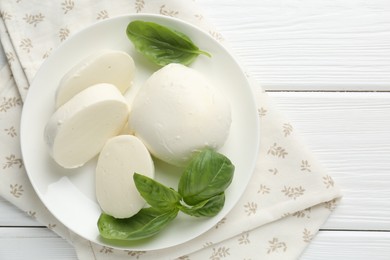 Photo of Pieces of delicious mozzarella cheese and basil on white wooden table, top view