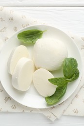 Photo of Pieces of delicious mozzarella cheese and basil on white wooden table, top view