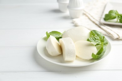 Photo of Pieces of delicious mozzarella cheese and basil on white wooden table. Space for text
