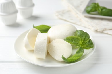 Photo of Pieces of delicious mozzarella cheese and basil on white wooden table, closeup