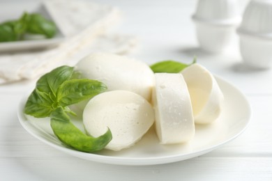 Photo of Pieces of delicious mozzarella cheese and basil on white wooden table, closeup