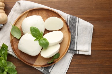 Photo of Pieces of delicious mozzarella cheese and basil leaves on wooden table, flat lay