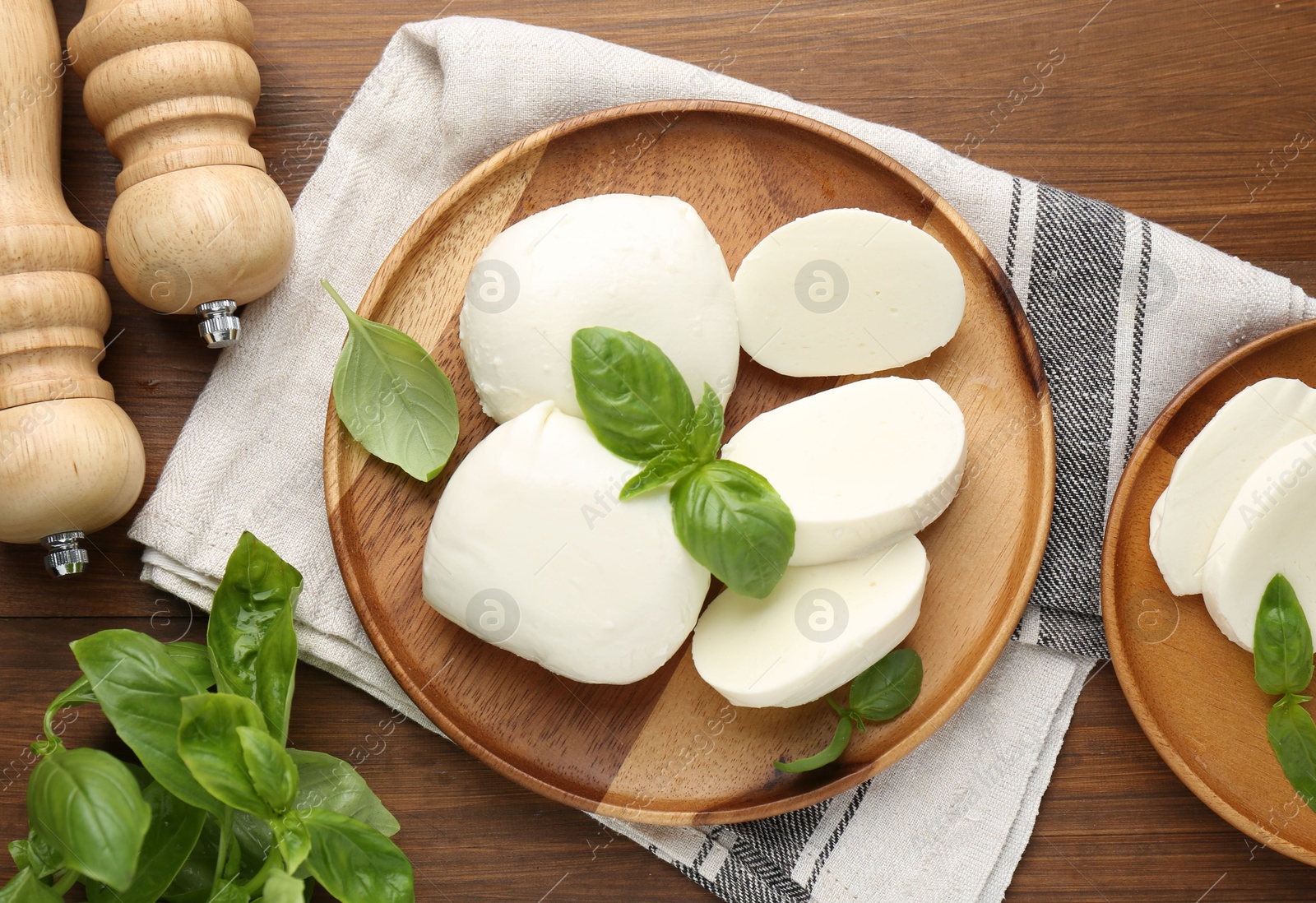 Pieces of delicious mozzarella cheese, basil leaves and shakers on wooden table, flat lay Photo of Pieces of delicious mozzarella cheese, basil leaves and shakers on wooden table, flat lay