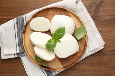 Photo of Pieces of delicious mozzarella cheese and basil leaves on wooden table, top view