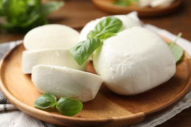 Photo of Pieces of delicious mozzarella cheese and basil leaves on wooden table, closeup
