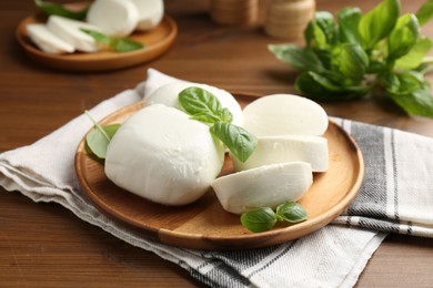 Photo of Pieces of delicious mozzarella cheese and basil leaves on wooden table, closeup