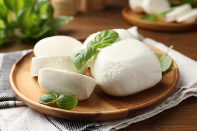 Photo of Pieces of delicious mozzarella cheese and basil leaves on wooden table, closeup